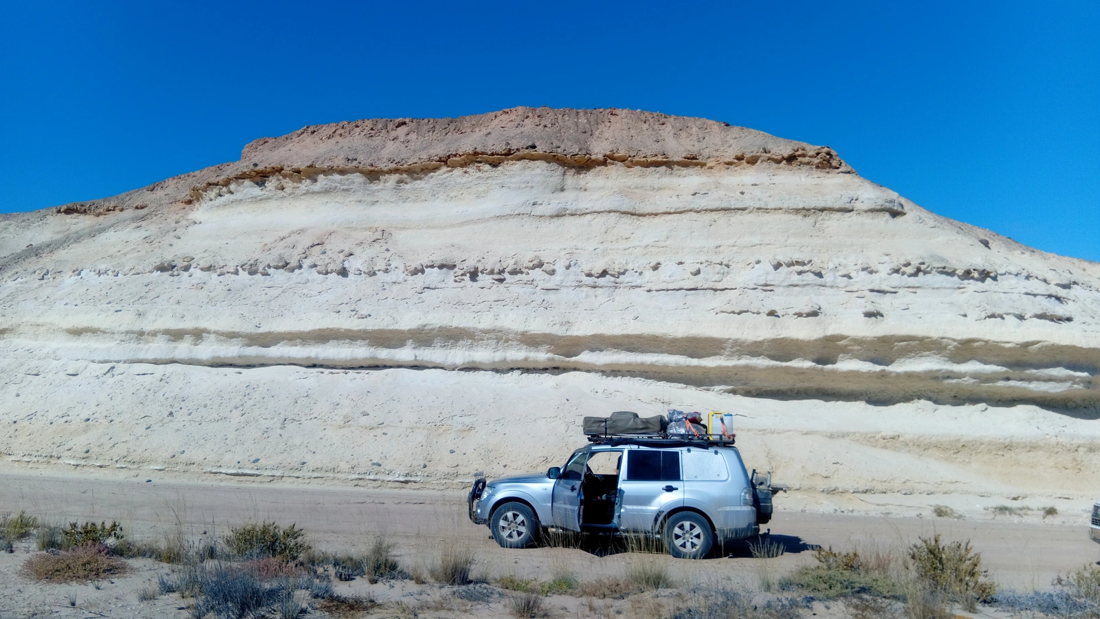 Silver expedition vehicle below pale desert cliffs