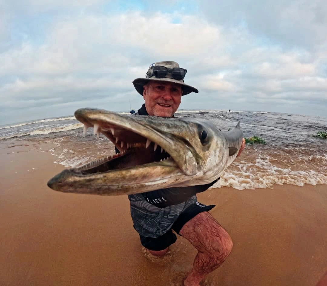 Angler holding a long fish on a sandy beach