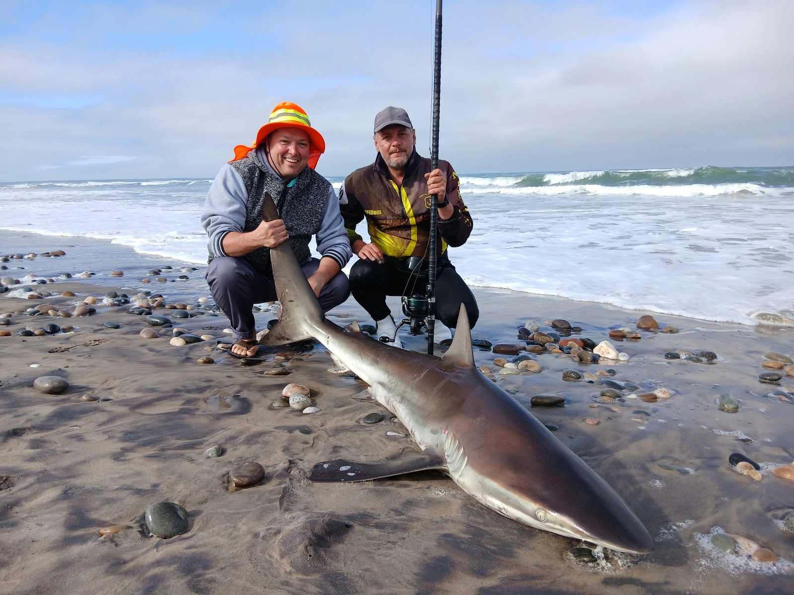 Two anglers beside a shark at the shoreline