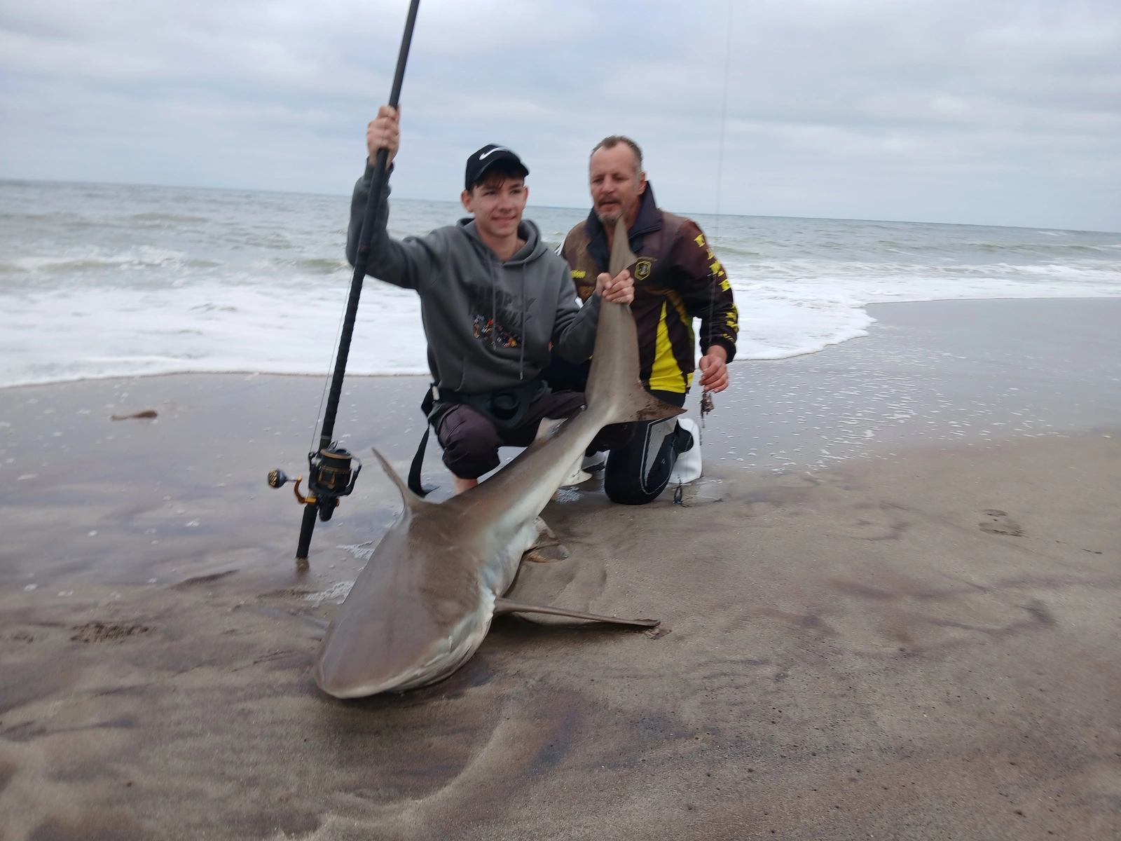Two anglers beside a shark on the beach
