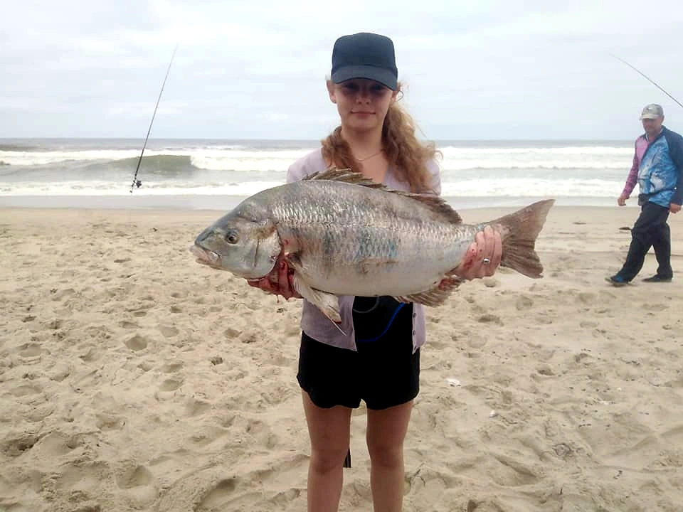Young angler holding a fish beside the sea