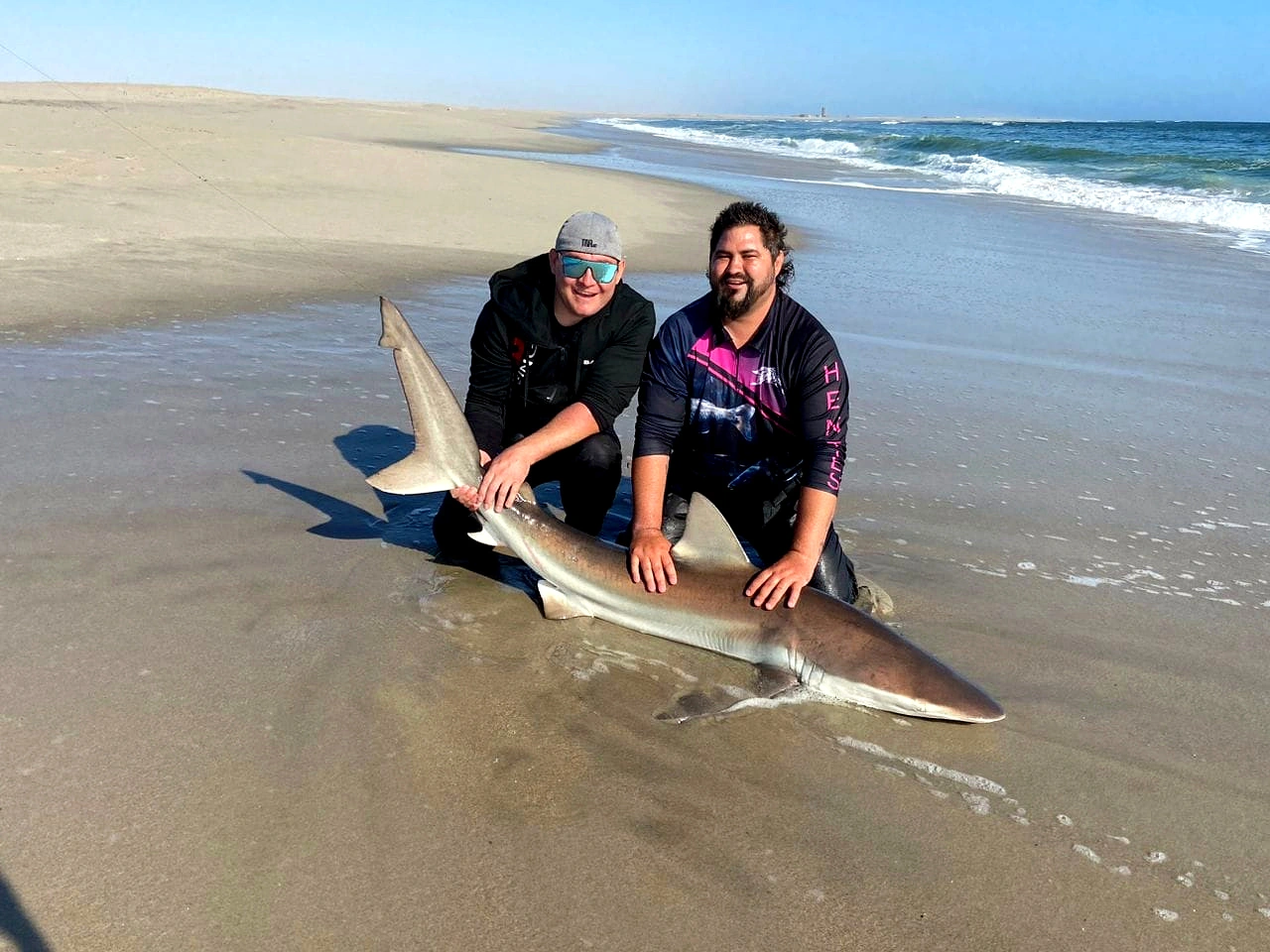 Two anglers beside a shark on a sandy beach